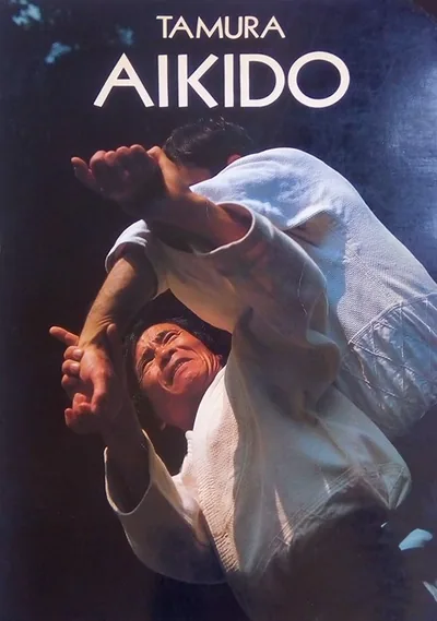 Cover of Aïkido (1986): “TAMURA” and “AIKIDO” in white capitals above a colour photo of a throw, two aikidoka in white keikogi against a dark background